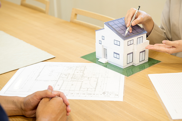 机の上に間取図を広げ小さな家の模型を使用しお客様へ説明しているスタッフの手元